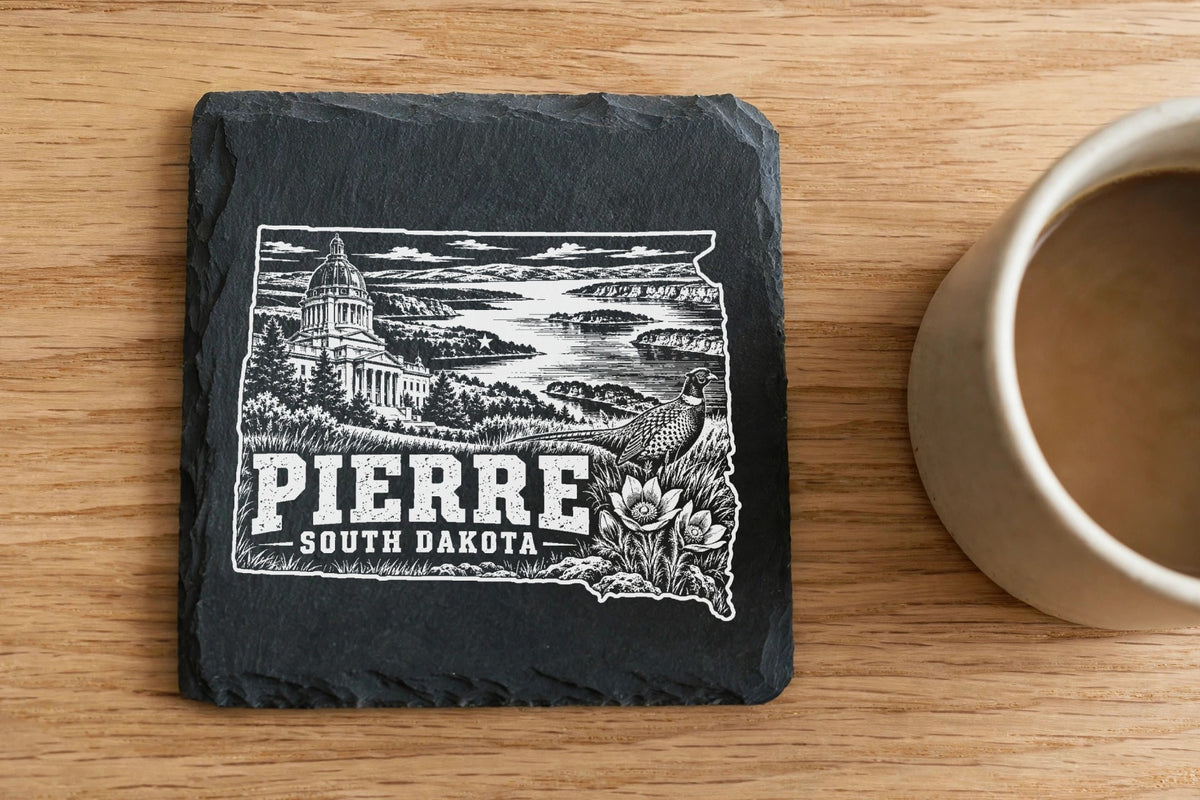 Square slate coaster with a white engraved design of Pierre, South Dakota, next to a coffee mug.