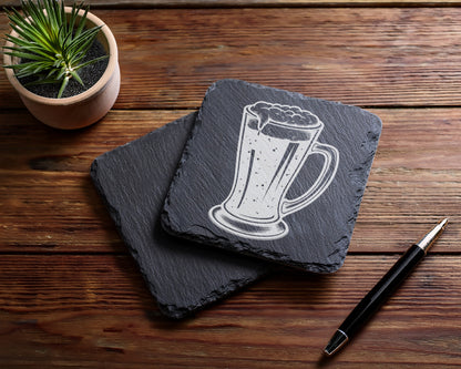 Two slate coasters, one with a beer mug etching, a plant, and a pen.