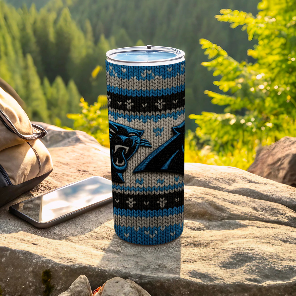 Carolina Panthers tumbler with knit pattern and logos on a rock with a backpack and phone.
