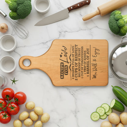 Wooden cutting board engraved with "Recipe for Love" and cooking ingredients.