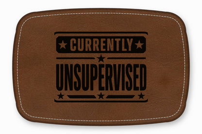 Brown leather patch with white stitching and the black text Currently Unsupervised.