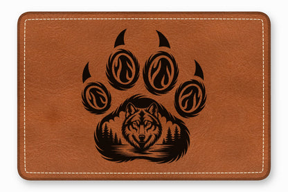 Brown rectangular leather patch with white border stitching and a black engraved wolf in a forest paw print graphic.