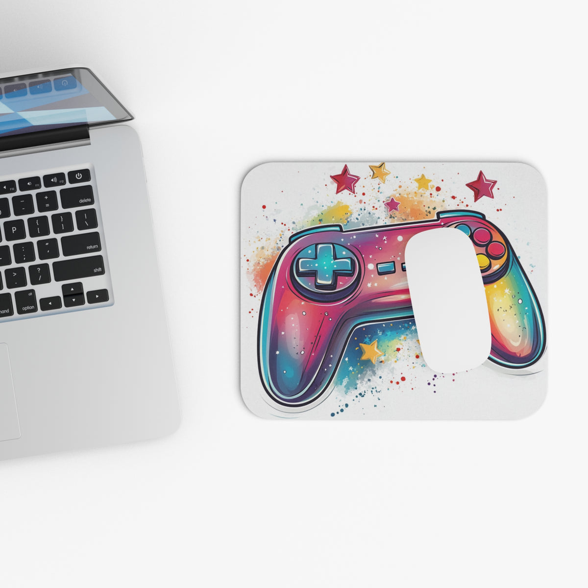 Colorful watercolor gamepad with stars design on a mousepad next to a laptop.