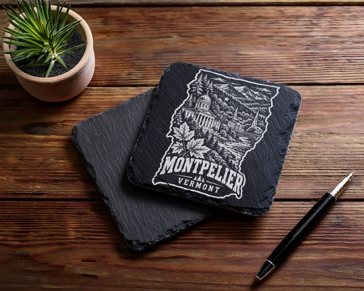 Two square slate coasters rest on a wooden table beside a potted succulent and a pen.