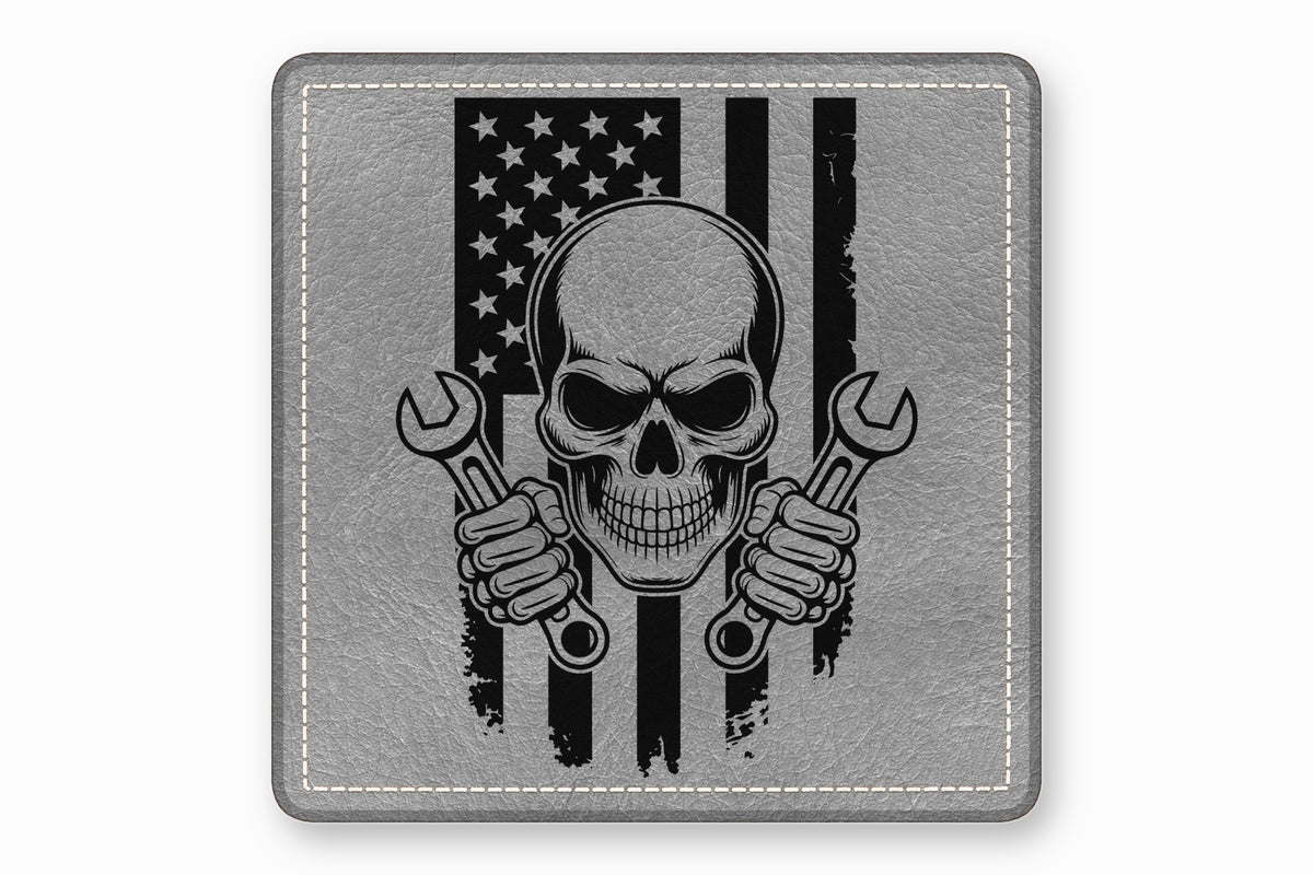 A square grey leather patch features a black skull holding wrenches in front of an American flag.