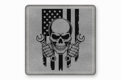 A square grey leather patch features a black skull holding wrenches in front of an American flag.