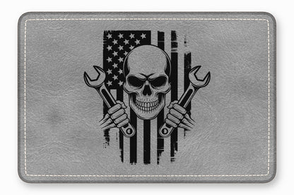 A grey leather patch with rounded corners features a black graphic of a skull holding two crossed wrenches over a distressed American flag.