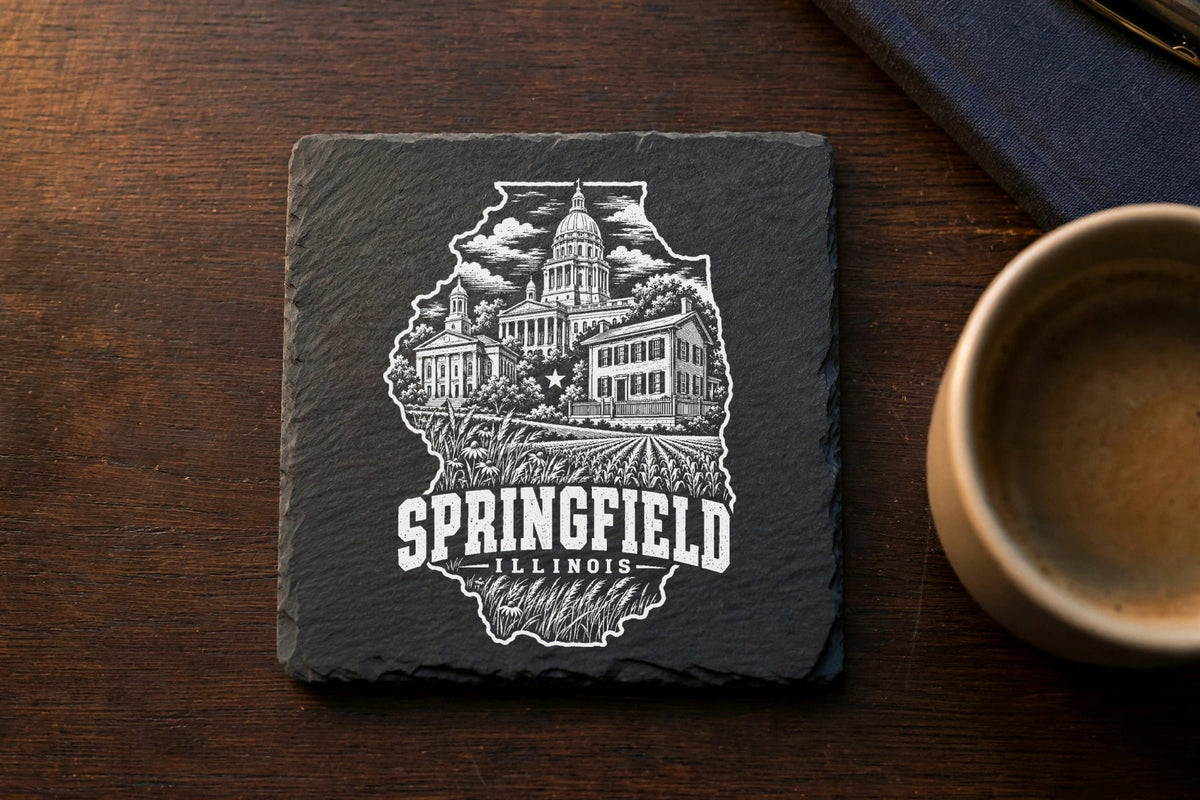 Square black slate coaster engraved with a Springfield Illinois landmark design on a wooden table.
