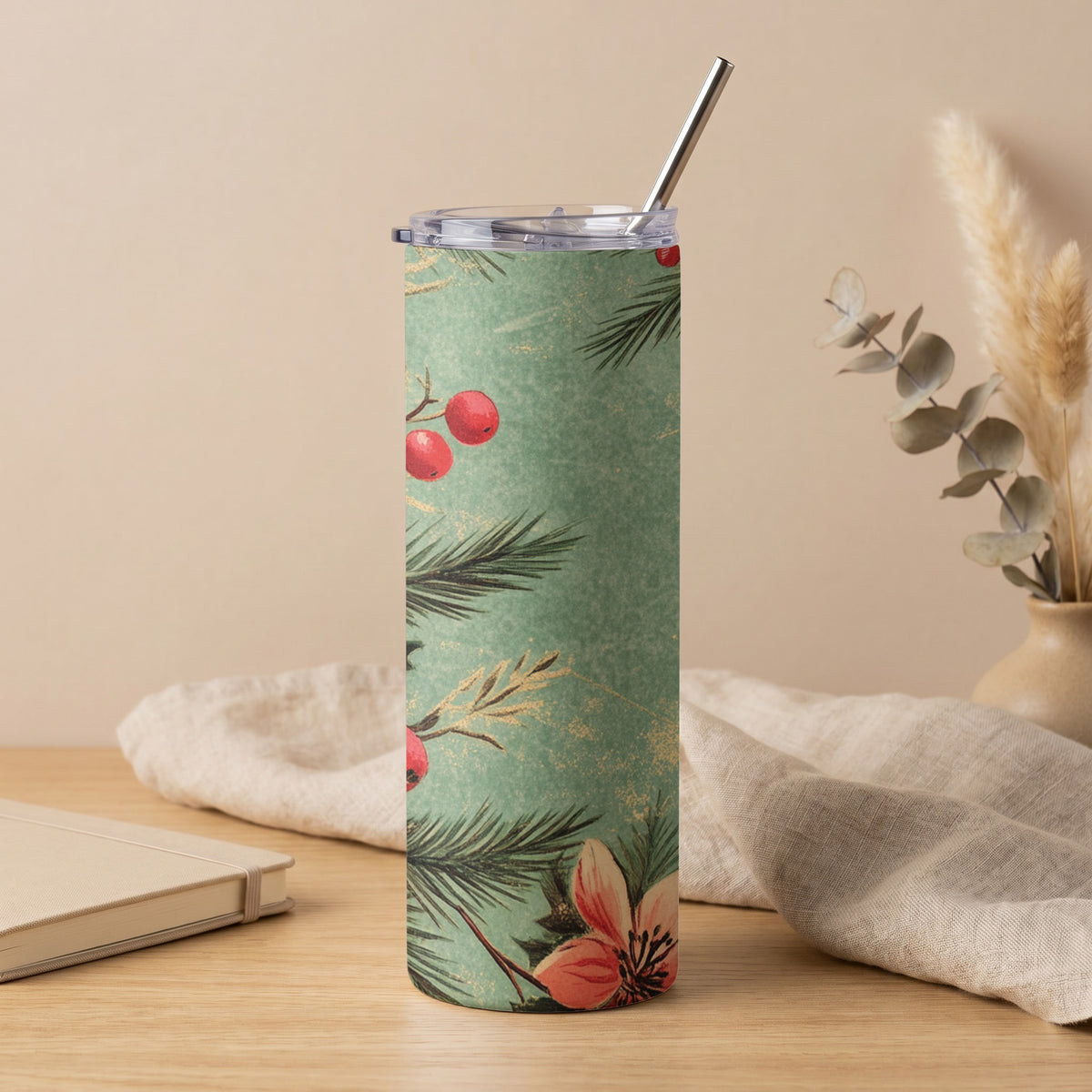 Green tumbler with red berries, pine needles, and flowers, and a metal straw.