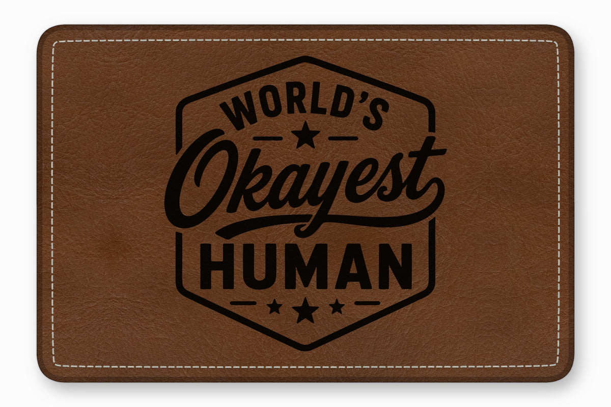 Brown leather patch with white stitching and the engraved text Worlds Okayest Human.