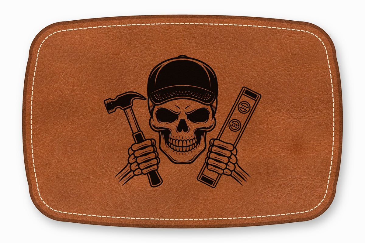 A brown leather patch featuring a black laser-engraved skull wearing a cap and holding a hammer and level.