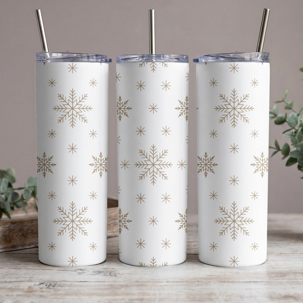 Three white tumblers with gold snowflake pattern and metal straws.
