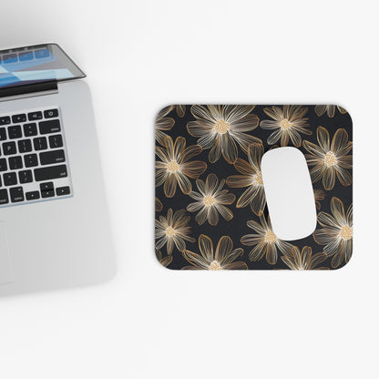 Mousepad with gold line art flowers on a dark background, next to a laptop.
