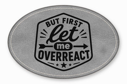 An oval gray faux leather patch with white stitched edges and black text reading "But first let me OVERREACT".