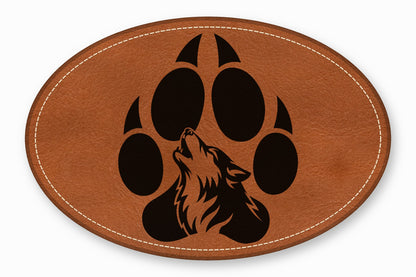 Oval brown leather patch with white stitched border featuring a black wolf silhouette inside a paw print.