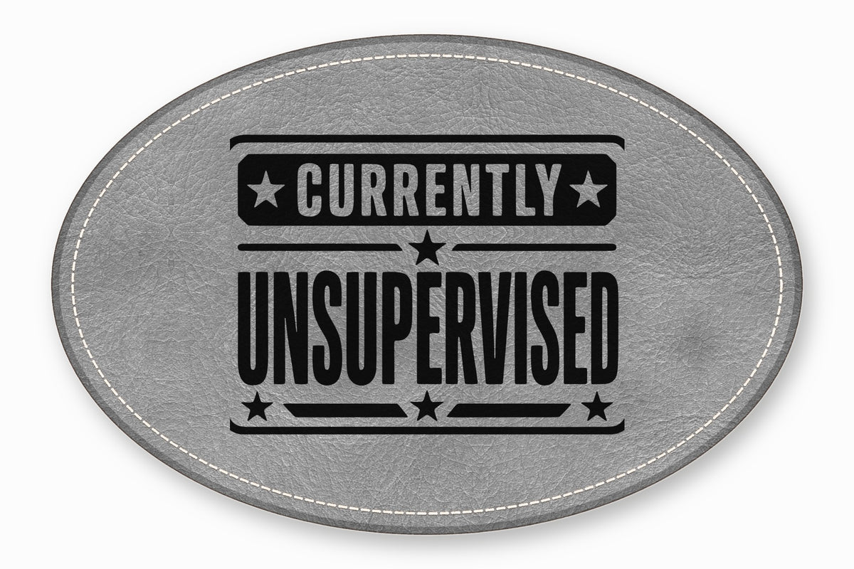An oval grey leather patch with white stitched edges and black text reading Currently Unsupervised.