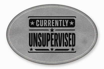 An oval grey leather patch with white stitched edges and black text reading Currently Unsupervised.