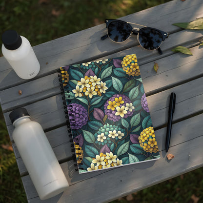 Spiral-bound notebook with a dark floral pattern featuring yellow, purple, and teal flowers.
