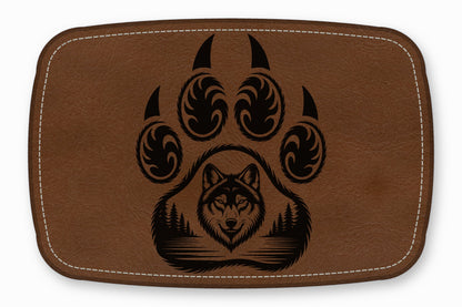 A brown leather patch features a black graphic of a bear paw containing a wolf and forest landscape.