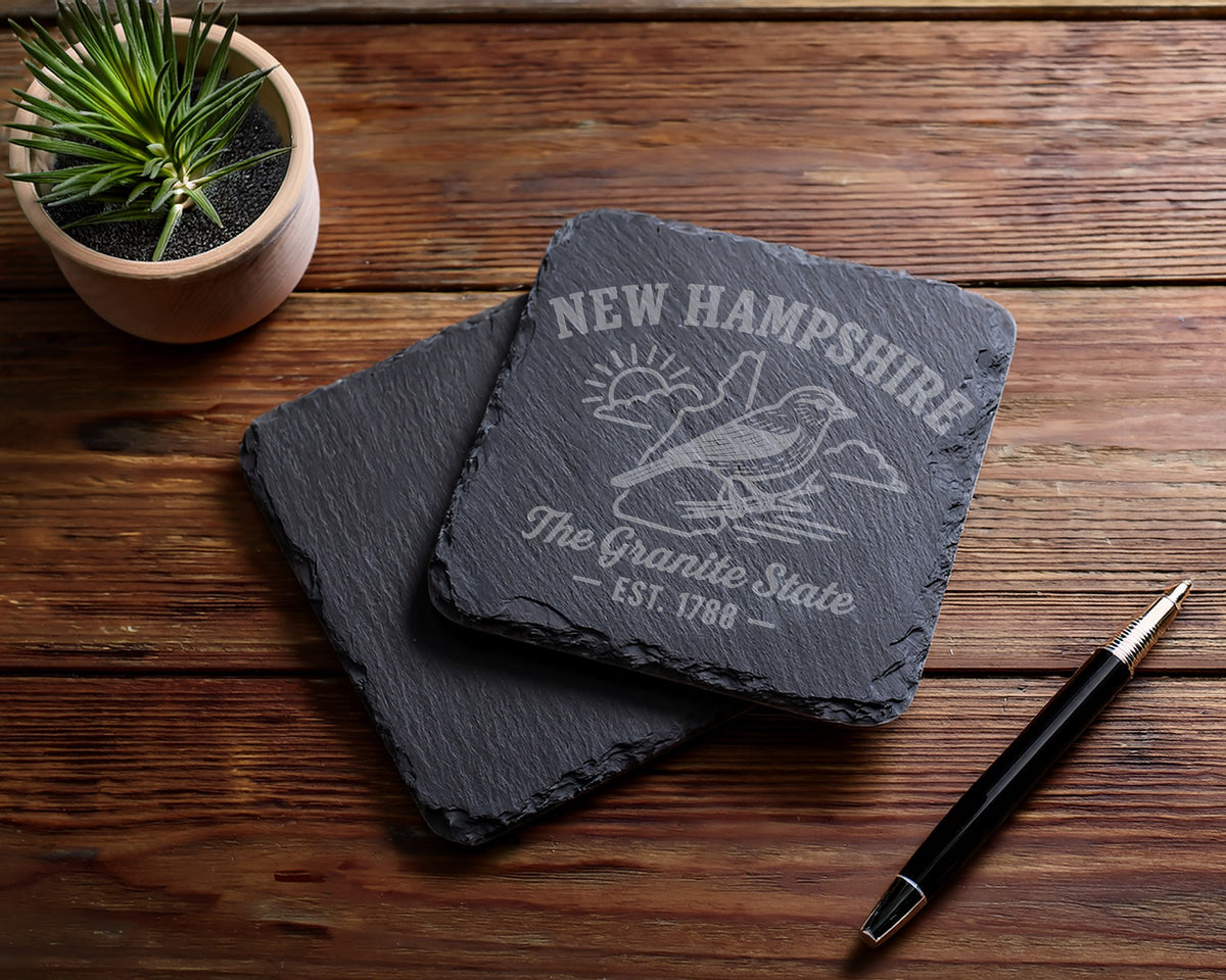 New Hampshire slate coasters engraved with a bird, sun, and "The Granite State - Est. 1788".