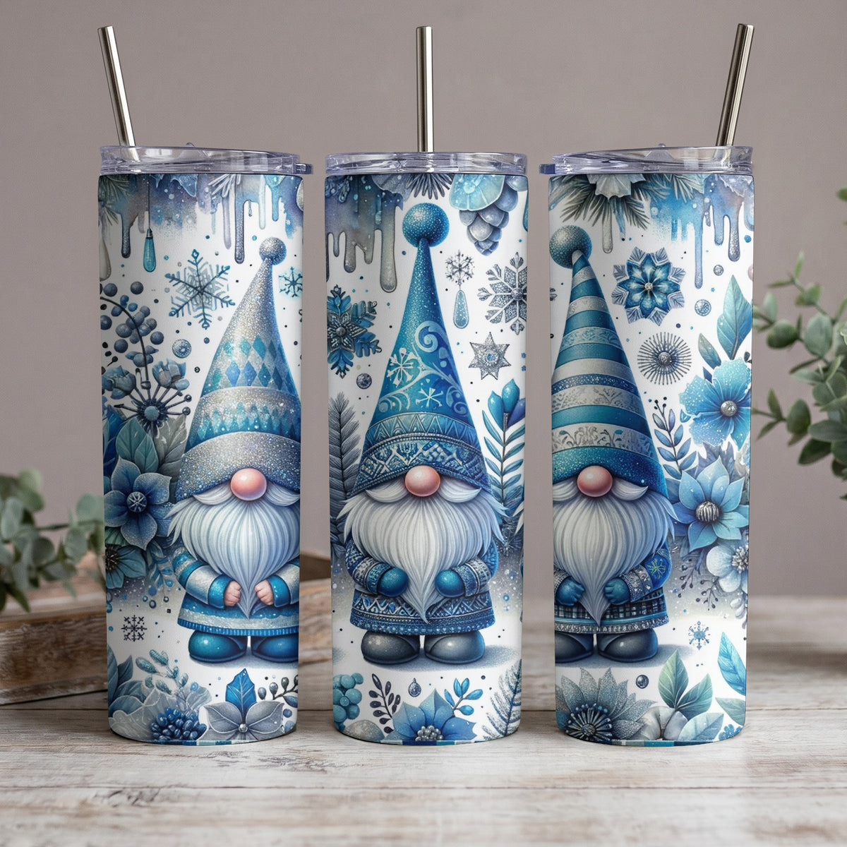 Three tumblers with blue and white gnome winter designs featuring snowflakes and flowers.