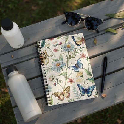 Spiral notebook with a botanical butterfly print, next to water bottles and sunglasses.