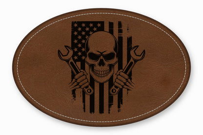 An oval brown leather patch with white stitching featuring a skull, crossed wrenches, and an American flag.