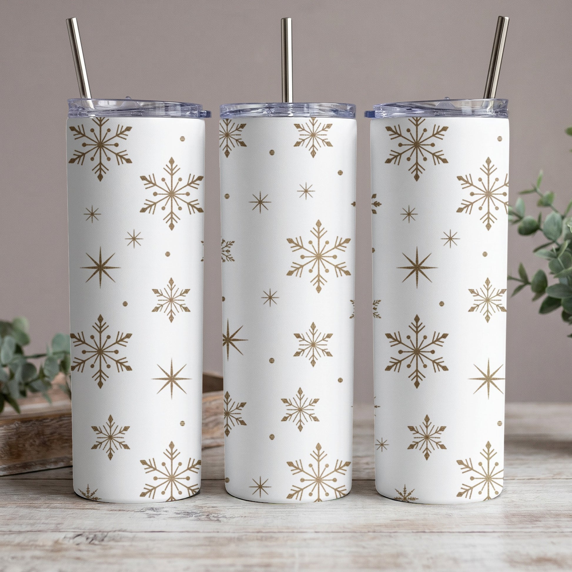 Three white tumblers with a gold snowflake pattern and silver straws.