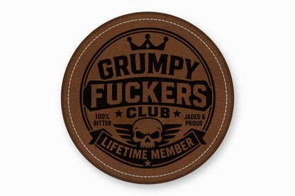 Round brown leather coaster featuring a stitched border and a black Grumpy Fuckers Club emblem.
