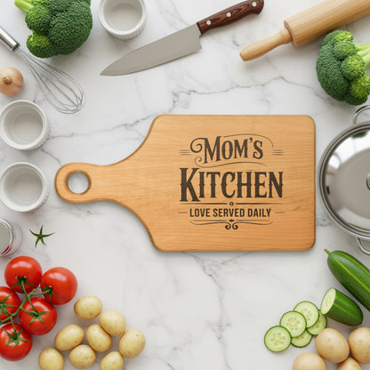 Wooden cutting board with "Mom's Kitchen" text, surrounded by fresh ingredients and kitchen tools.