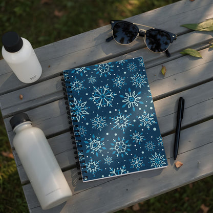 Spiral notebook with a blue snowflake pattern rests on a wooden bench with water bottles and sunglasses.