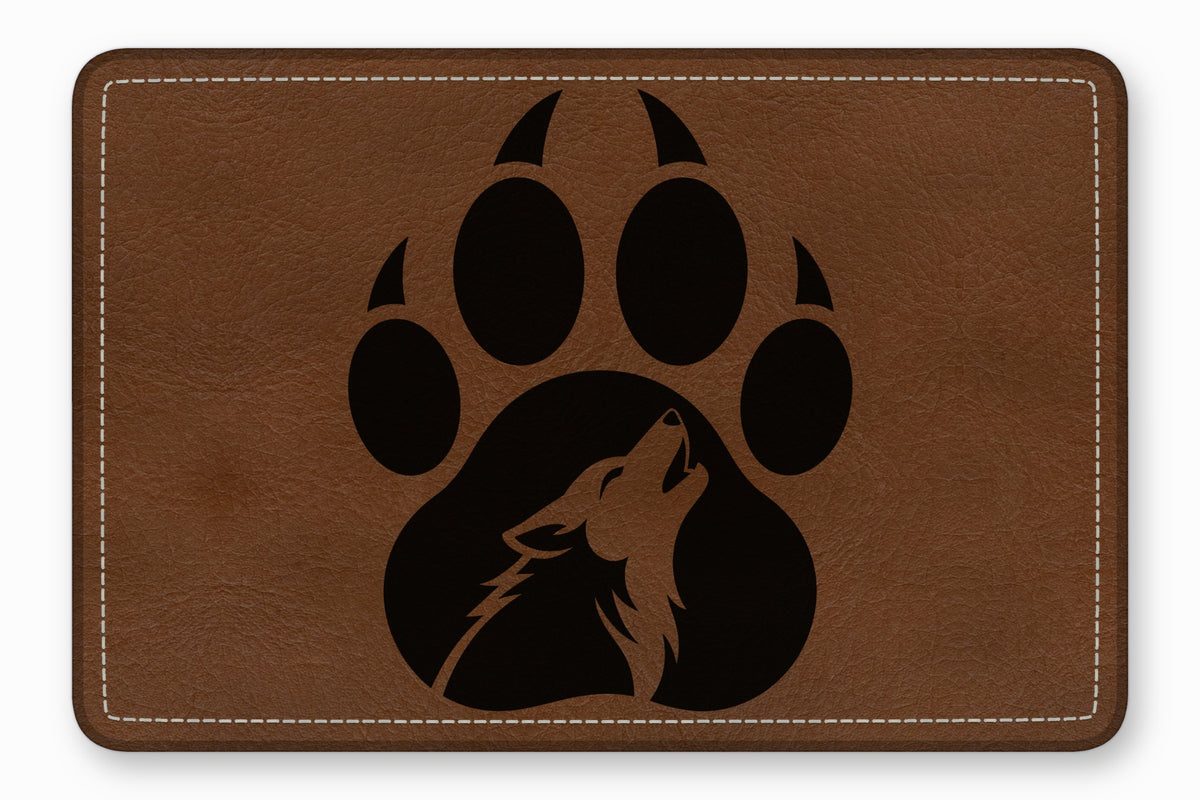 Brown leather rectangular patch with white stitched border and a black paw print containing a howling wolf silhouette.