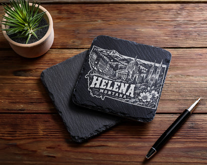 Two square black slate coasters featuring a white engraved Helena Montana skyline design on a wooden table.