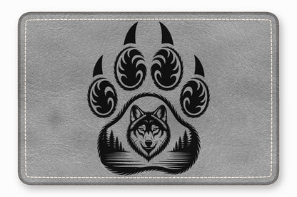 Grey rectangular leather patch with rounded corners featuring a black engraved paw print containing a wolf and forest design.