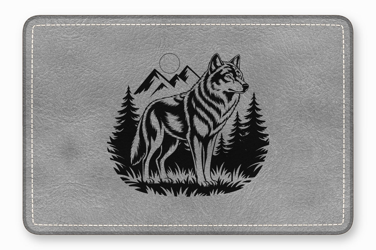 A gray leather desk mat with a black engraved design of a standing wolf, mountains, and pine trees.