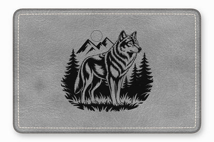A gray leather desk mat with a black engraved design of a standing wolf, mountains, and pine trees.
