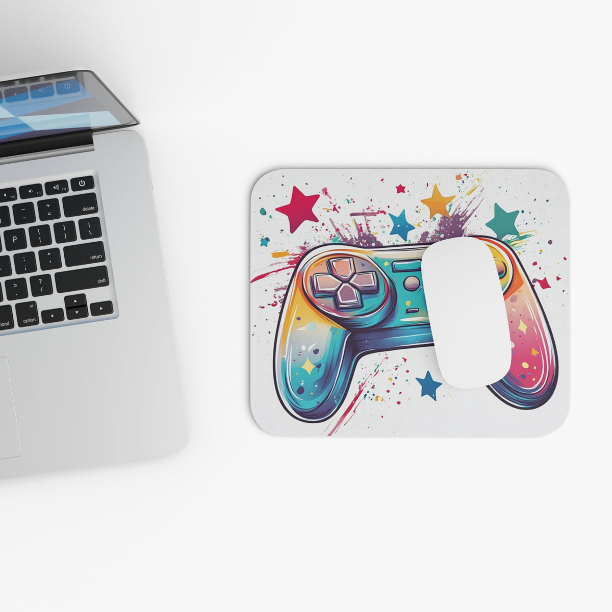 Colorful video game controller and stars on a white mousepad next to a laptop.