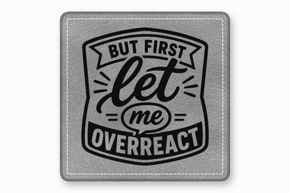 Square grey leather patch with white stitched border, featuring the black text But First Let Me Overreact.