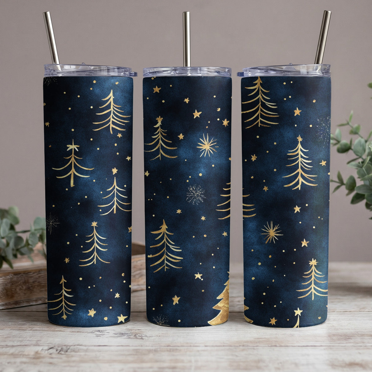 Three dark blue tumblers with gold Christmas trees and stars pattern and metal straws.