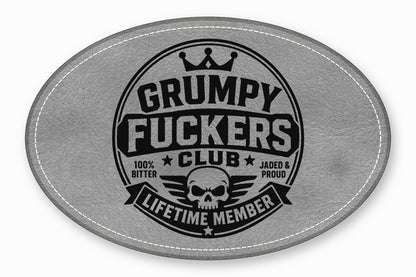 Oval grey leather patch with white stitched border featuring a black emblem with a skull, crown, and text.