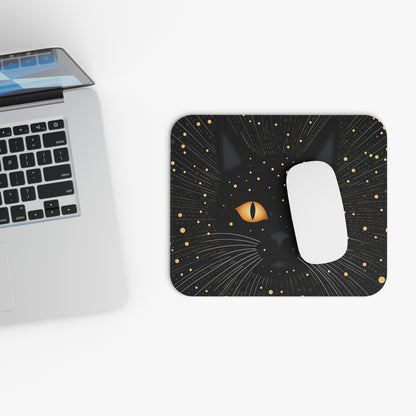 Black cat face with orange eyes on a mousepad next to a laptop.