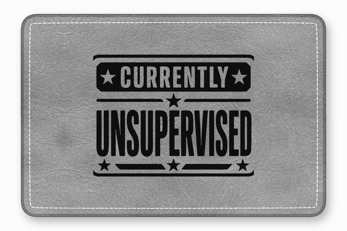 A rectangular gray faux leather patch featuring white stitching along the border and black text reading Currently Unsupervised.