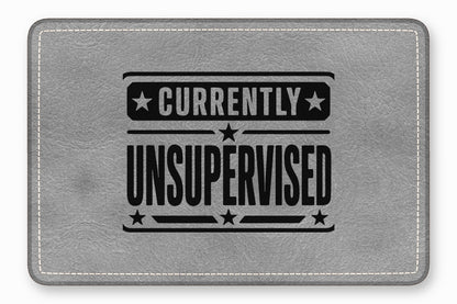 A rectangular gray faux leather patch featuring white stitching along the border and black text reading Currently Unsupervised.