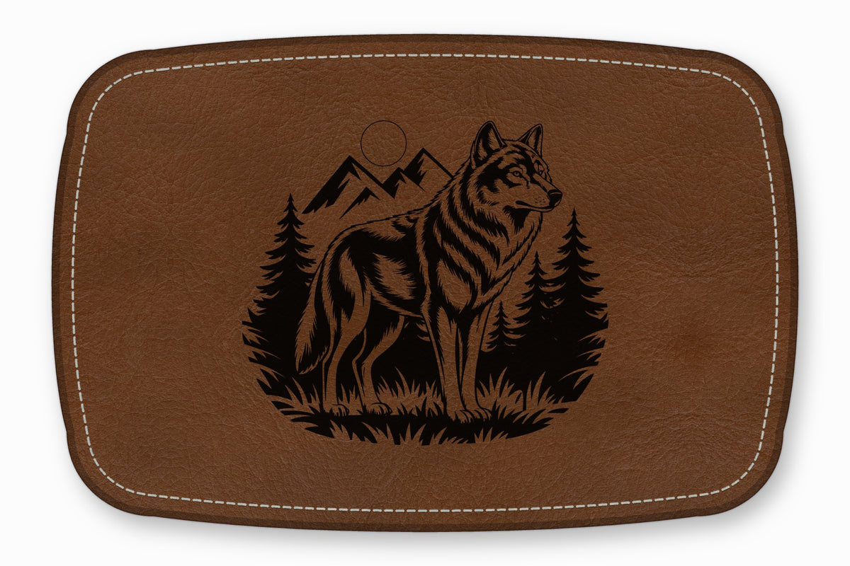 Brown leather patch featuring a laser-engraved design of a wolf standing before pine trees and mountains.
