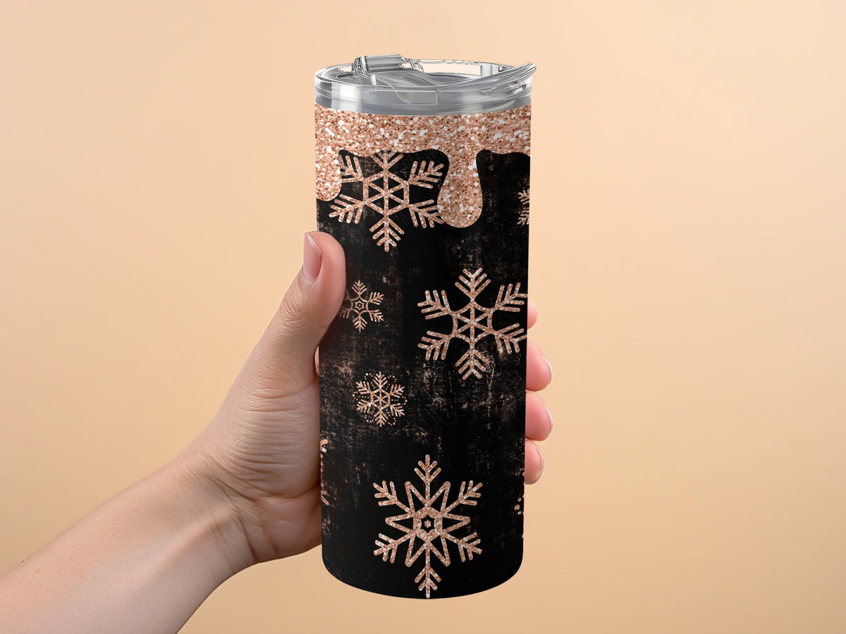Black tumbler with rose gold glitter drips and snowflake pattern held by a hand.