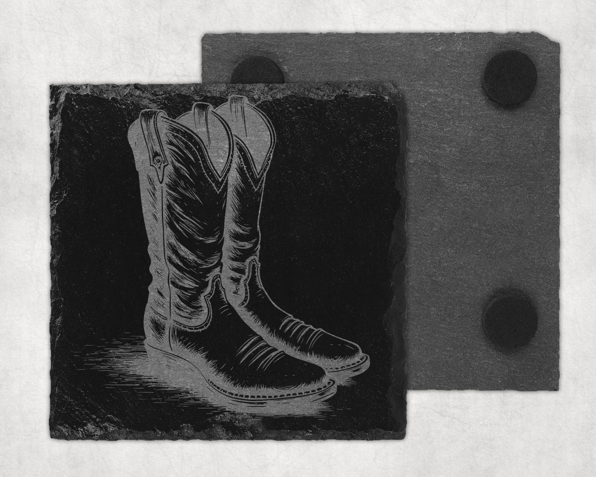 Engraved cowboy boots on a black slate coaster with a second slate coaster behind.