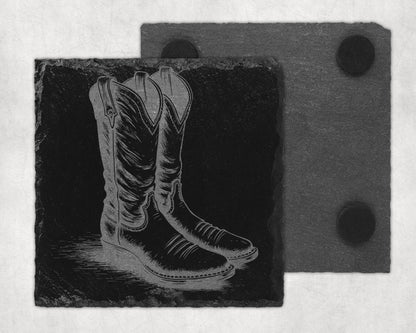 Engraved cowboy boots on a black slate coaster with a second slate coaster behind.