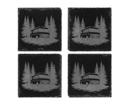 Four square black slate coasters featuring an engraved design of a camper van parked among pine trees.