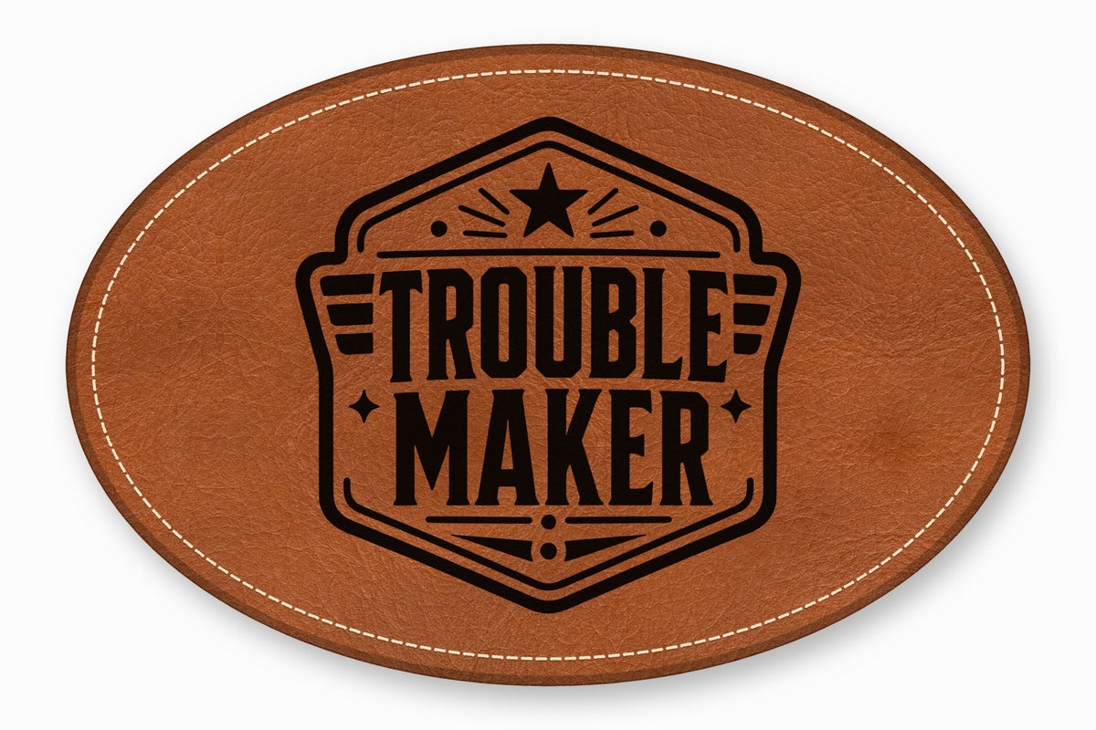 An oval brown leather patch featuring white stitching along the edge and a black printed emblem with the text Trouble Maker.