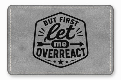 Gray faux leather patch with white stitched border and black printed text reading BUT FIRST let me OVERREACT.
